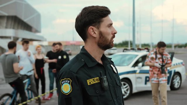 Portrait of professional policeman staying in road accident area outdoors. Close-up handsome cop speaking by walkie talkie calling for reinforcement. Crime in the city.