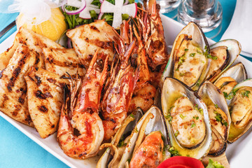European cuisine, Mediterranean dish. Plate with assorted sea grill. Fried fish, king prawns with lemon, mussels with oyster sauce, colmar rings, crab meat