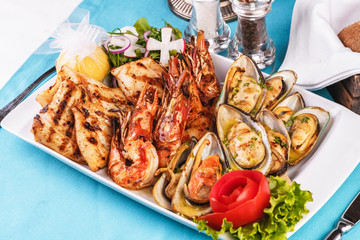 European cuisine, Mediterranean dish. Plate with assorted sea grill. Fried fish, king prawns with lemon, mussels with oyster sauce, colmar rings, crab meat