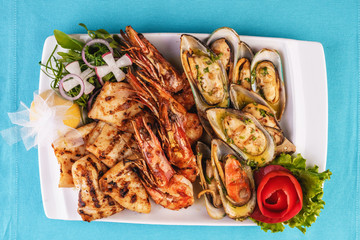 European cuisine, Mediterranean dish. Plate with assorted sea grill. Fried fish, king prawns with lemon, mussels with oyster sauce, colmar rings, crab meat
