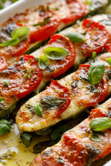 Baked, stuffed zucchini with the addition of tomatoes, mozzarella cheese, fresh basil and olive oil (caprese salad) in a ceramic baking dish, close-up, top view. Nutritious and tasty vegetarian dish