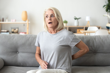 Mature woman sitting on couch suffers from back pain