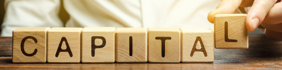 A man puts wooden blocks with the word Capital. The combination of material, intellectual and...