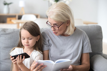 Serious grandma and little granddaughter sitting on couch