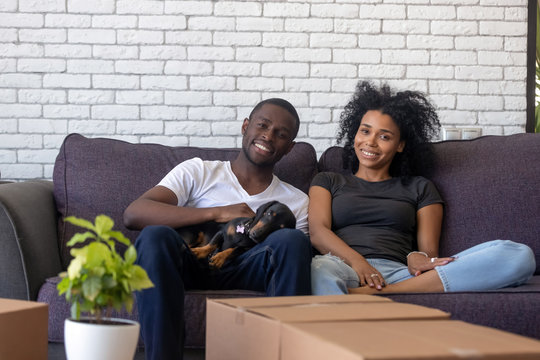 Happy african couple resting on couch with dog at home
