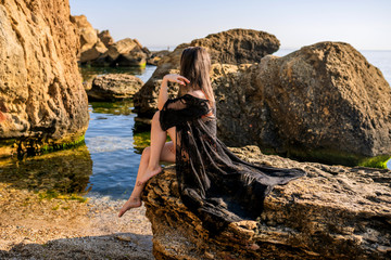 Beautiful tanned girl sitting on a big stone by the sea