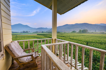 Balcony home exterior with chairs and decoration in contemporary home. Morning corn field scene at sunrise.