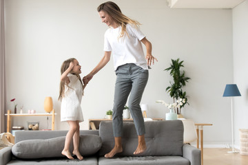 Cheerful mother and daughter jumping on couch at home