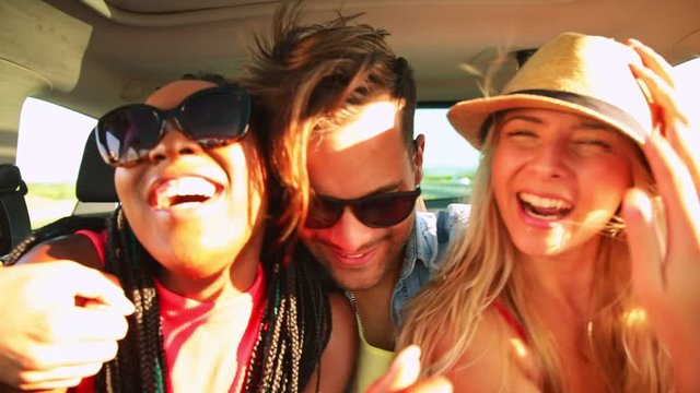 Three best friends enjoying traveling in the car, sitting in rear seat and having lots of fun making selfie on a road trip.