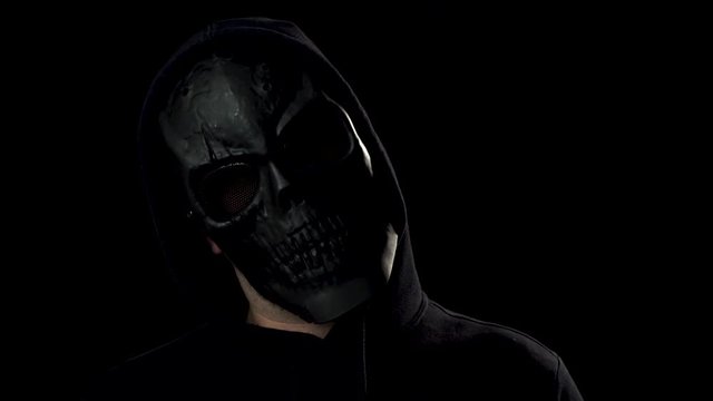 Portrait of spooky man in black skull mask looking in camera and scary you