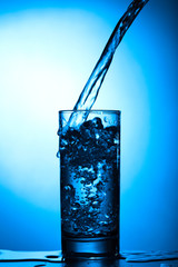 Pure water with bubbles pours into the glass on a blue background
