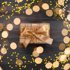 Obraz na płótnie Canvas Golden heart shaped confetti and wrapped gift on dark wooden background, copy space