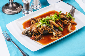Seafood, Mediterranean cuisine, European dish. Fish stewed in tomato sauce with onion rings, mushrooms, herbs and vegetables. Caucasian national cuisine