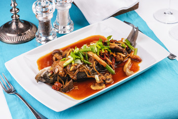 Seafood, Mediterranean cuisine, European dish. Fish stewed in tomato sauce with onion rings, mushrooms, herbs and vegetables. Caucasian national cuisine