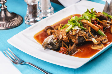 Seafood, Mediterranean cuisine, European dish. Fish stewed in tomato sauce with onion rings, mushrooms, herbs and vegetables. Caucasian national cuisine