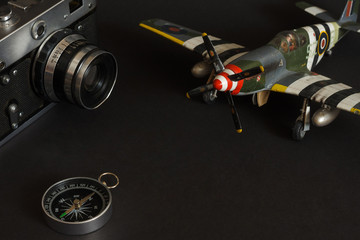 Still life with a scale model of a aircraft fighter, old analog film camera and compass. Dark background	