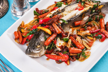Seafood, Mediterranean cuisine, European dish. Whole fish baked with tomatoes with onion rings, red and green peppers, chili peppers, greens and vegetables. Caucasian national cuisine