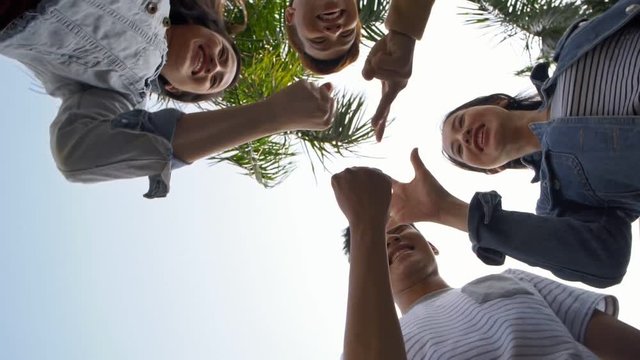 Directly below view of four Asian teenagers standing in circle, playing game with their hands and fingers and laughing