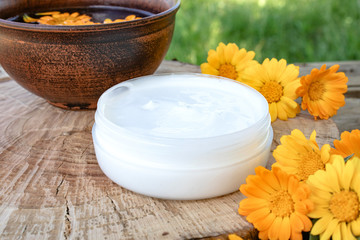 Obraz na płótnie Canvas Nourishing cream with calendula extract with fresh calendula flowers on a wooden background in nature.