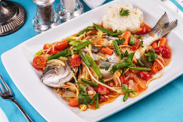 Seafood, Mediterranean cuisine. Baked sea fish with mushrooms, herbs, carrots, millers, cilantro, corn and onions. Caucasian national cuisine