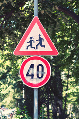 School zone warning road and 40 speed limit signs against green park trees bokeh background