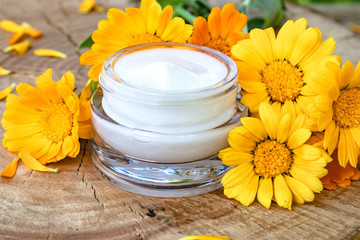 Fototapeta na wymiar A jar of white cosmetic cream for body care. Fresh orange calendula flowers on wooden background.