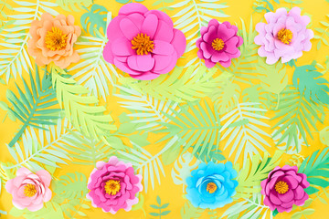 flat lay with paper cut multicolored flowers on tropical leaves on yellow bright background with copy space