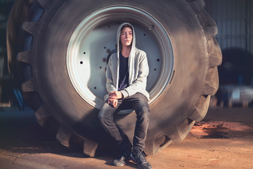 portrait of a smiling young man sitting in a huge wheel of a tractor