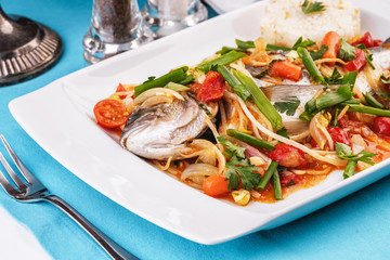 Seafood, Mediterranean cuisine. Baked sea fish with mushrooms, herbs, carrots, millers, cilantro, corn and onions. Caucasian national cuisine