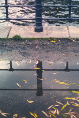 railing of a canal mirroring in a puddle with autumn leaves