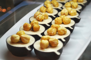 Sweet dessert with fresh hazelnuts and cream inside a chocolate shortcake, selective focus. A batch of cakes for sale displayed in the window of a bakery.