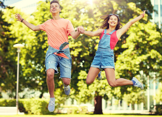 Fototapeta premium holidays, vacation, love and people concept - happy smiling teenage couple jumping at summer park