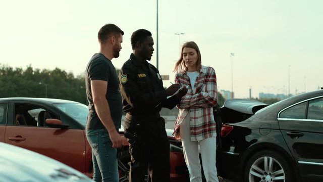 Police talking with the drivers at car accident area. Outdooor view of young people argue about bad situation near the broken cars. Police patrol.