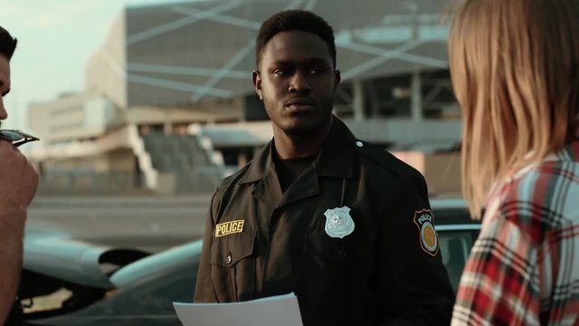 Serious afro-american policeman talking with the girl driver about a car accident. Attentive cop listening to the woman trying to help her. Police in action.