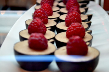 Raspberry dessert: sweet mousse inside a chocolate shortcake, selective focus. A fresh raspberry on top. A batch of cakes for sale displayed in the window of a bakery.