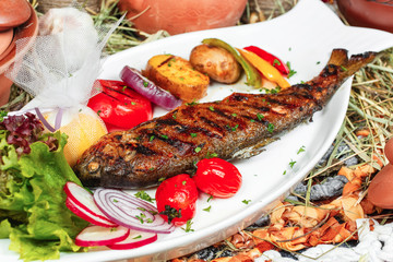 Mediterranean dish, Georgian recipe. Baked river fish with lemon, vegetables, pepper and grilled tomatoes with spices.