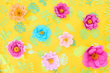top view of paper cut bright flowers with green tropical leaves on yellow bright background