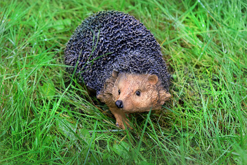 Decorative cute hedgehog garden decor. Beautiful Ceramic statue hedgehog on green grass in garden. Garden statue of hedgehog stands in summer lawn. soft selective focus