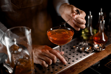 Bartender puts olive in glass with cocktail