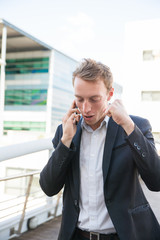 Happy business man with mobile phone excited with success. Joyful young professional standing near city building, talking on cell and making winner gesture. Business success concept