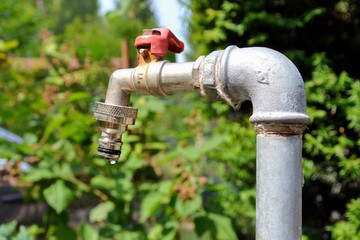 A tap with a drop of water against green park or garden background. Old outdoor brass tap....