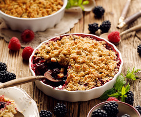 Crumble, Mixed berry (blackberry, raspberry) crumble, stewed fruits topped with crumble of oatmeal, almond flour, butter and sugar  in a baking dish on a wooden table, close-up - 280384055