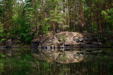 Fototapeta na wymiar Coniferous forest is reflected in a lake with granite shores
