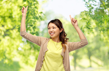 people and leisure concept - happy young asian woman dancing over green natural background