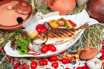 Mediterranean dish, European cuisine. whole fish baked in the oven, served with steamed vegetables - cauliflower, broccoli, carrots, cherry tomatoes and lemon