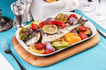 Mediterranean dish, Georgian recipe. Baked river fish with lemon, vegetables, pepper and grilled tomatoes with spices.