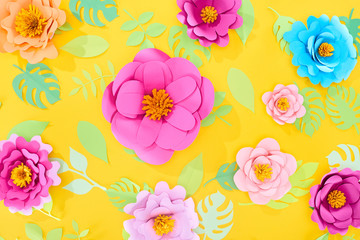 top view of paper cut flowers with green tropical leaves on yellow bright background