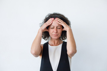 Unhappy woman suffering from headache. Middle aged woman with hands on heat standing with closed eyes isolated on grey background. Emotion concept