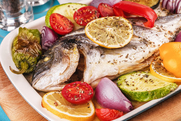 Mediterranean dish, Georgian recipe. Baked river fish with lemon, vegetables, pepper and grilled tomatoes with spices.
