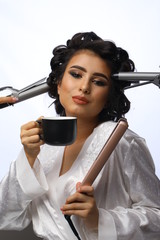 Beautiful joyful model with coffee is surrounded by many hands holding  hair iron, hair levelers and curler. Beauty and hair care concept. Concept of professional hair products.